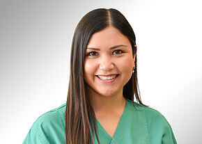 Jessica Wiesheier Porträt einer jungen Frau in grüner Pflege- bzw. OP-Kleidung, die freundlich in die Kamera lächelt. Neutraler, heller Hintergrund. Fokus auf ihr Gesicht und die medizinische Berufskleidung, suggeriert Gesundheitsberuf.