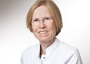 Prof. Dr. med. Regine Gätje Porträt einer lächelnden Person mit Brille in weißem Arztkittel vor neutralem Hintergrund; Kopf- und Schulteraufnahme.
