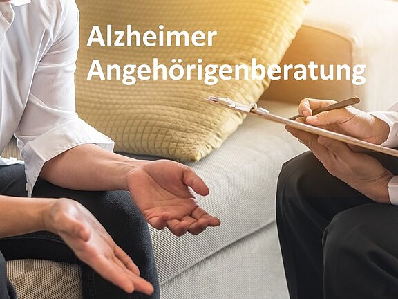 Zwei Personen sitzen auf einem Sofa im Beratungsgespräch; eine Person spricht mit geöffneten Händen, die andere macht Notizen auf einem Klemmbrett. Text im Bild: „Alzheimer Angehörigenberatung“. Thema: Unterstützung und Beratung für Angehörige.